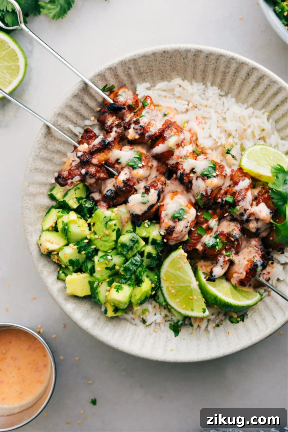 The Best Bang Bang Chicken Skewers Recipe Golden brown Bang Bang Chicken Skewers arranged on a bed of fluffy white rice, generously drizzled with Bang Bang sauce, and accompanied by a refreshing cucumber avocado salad. The presentation is vibrant and inviting.