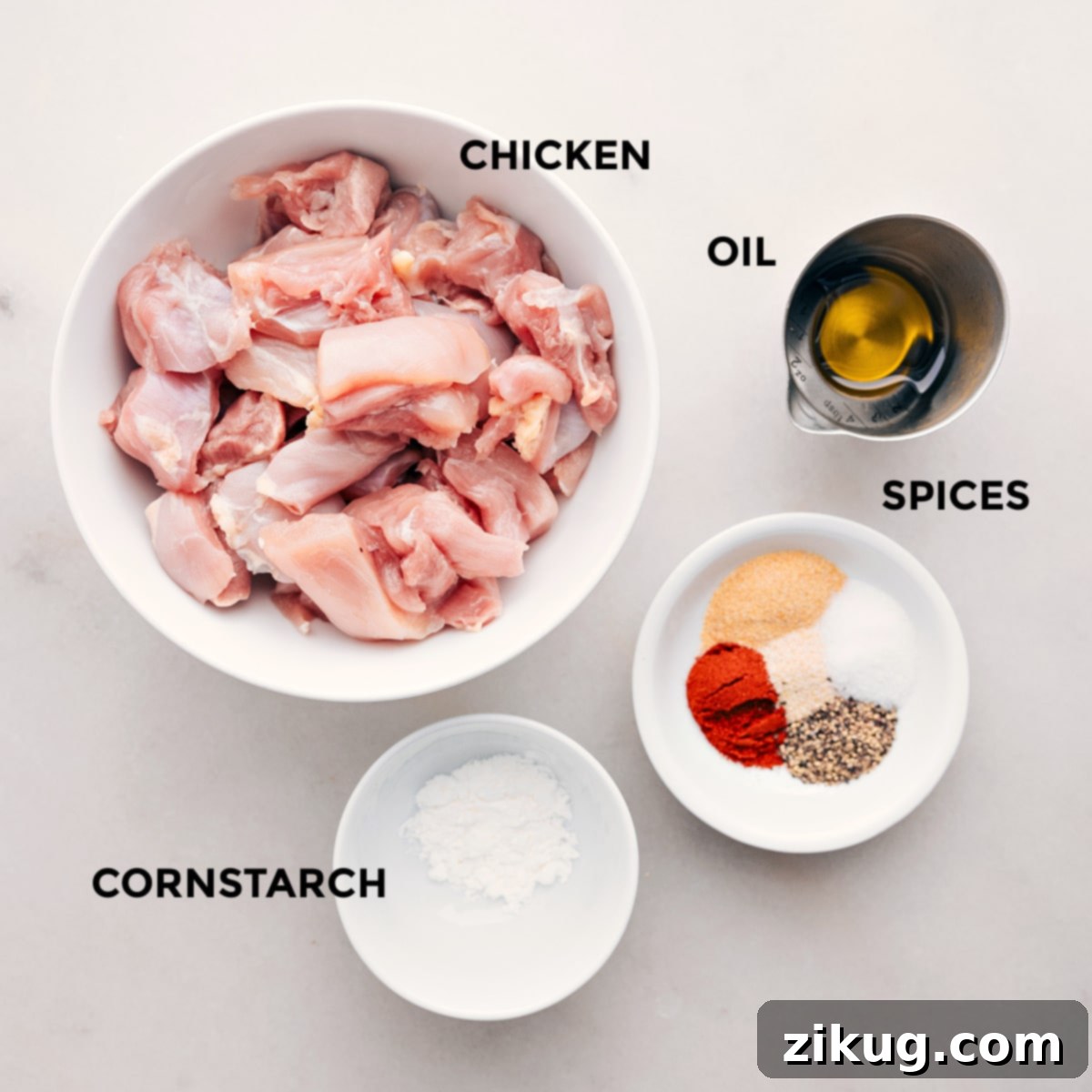 Ingredients In Bang Bang Chicken Skewers Raw chicken pieces are meticulously prepped with a blend of vibrant spices, olive oil, and cornstarch in a bowl, showcasing the initial steps for seasoning the meat before cooking.
