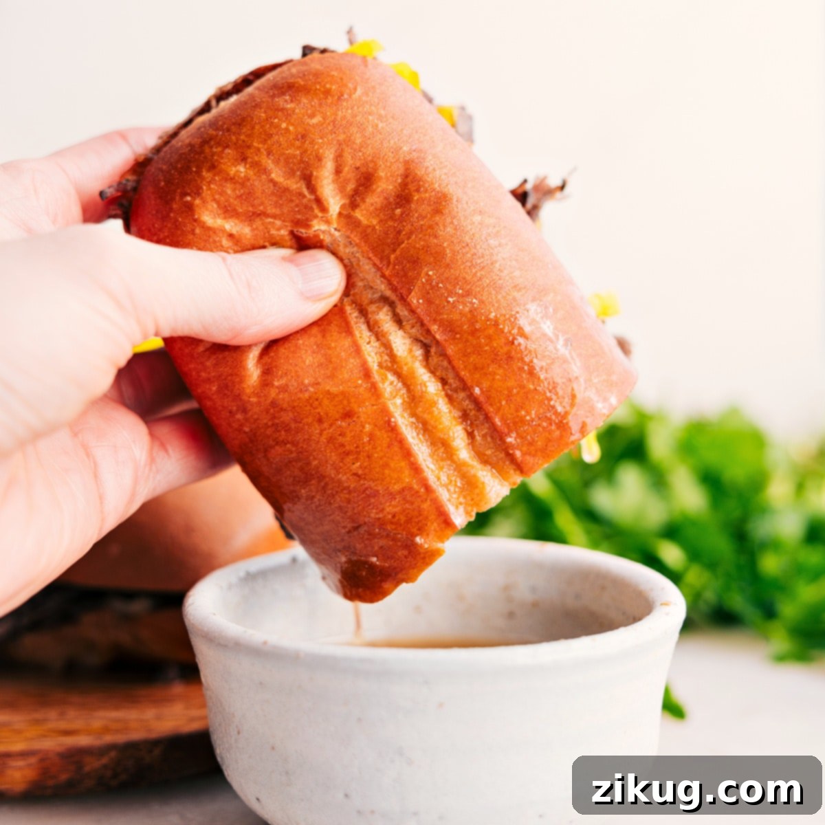 The Essential Italian Beef Sandwich Dip An Italian beef sandwich dipping into a small bowl of rich, savory broth from the slow cooker.
