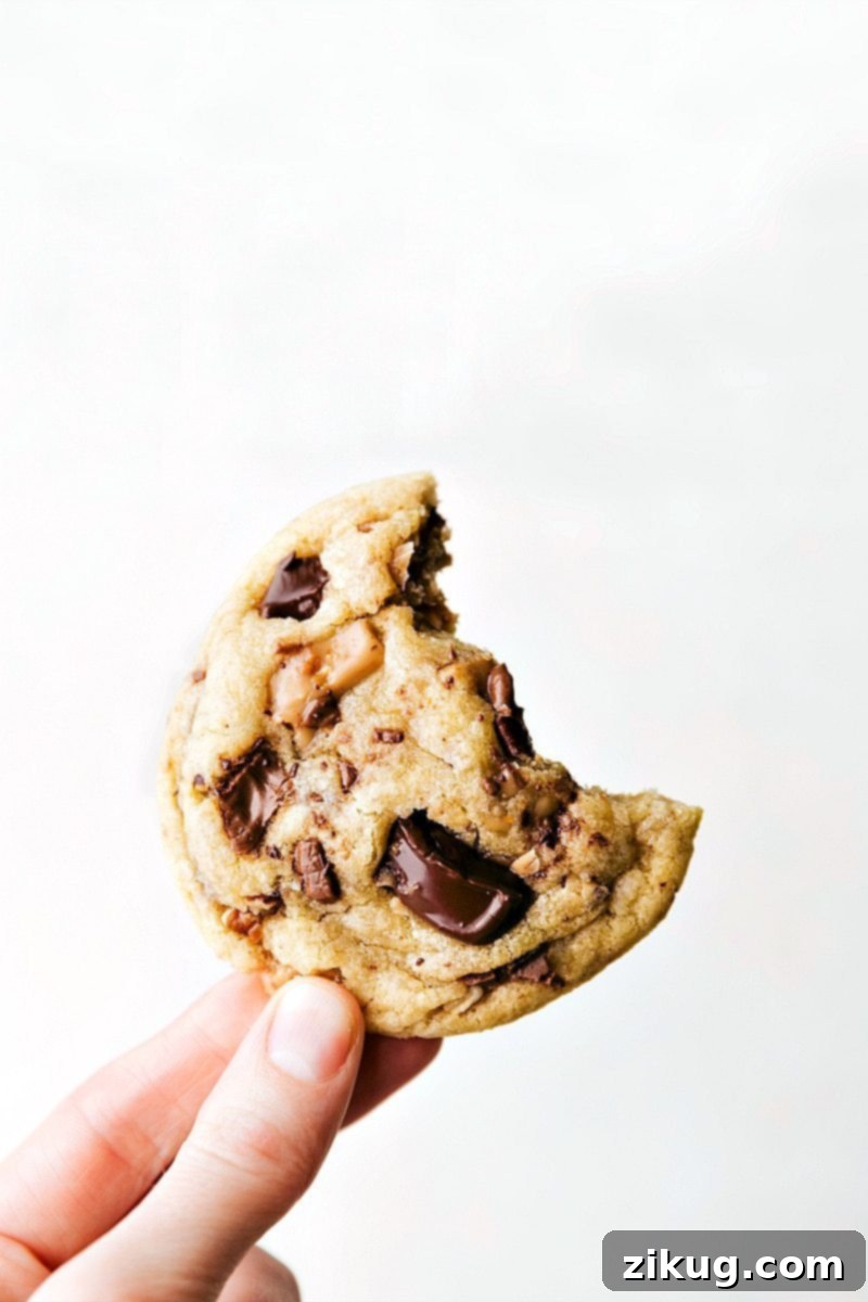 A toffee cookie being held with a bite taken out, showcasing its delightful texture.