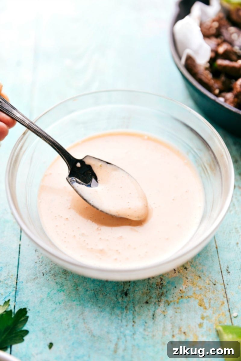 Dipping sauce only makes these Easy Asian Steak Bites even better! An overhead view of the creamy sriracha-lime dipping sauce in a small bowl, garnished with a lime slice, ready for dipping.
