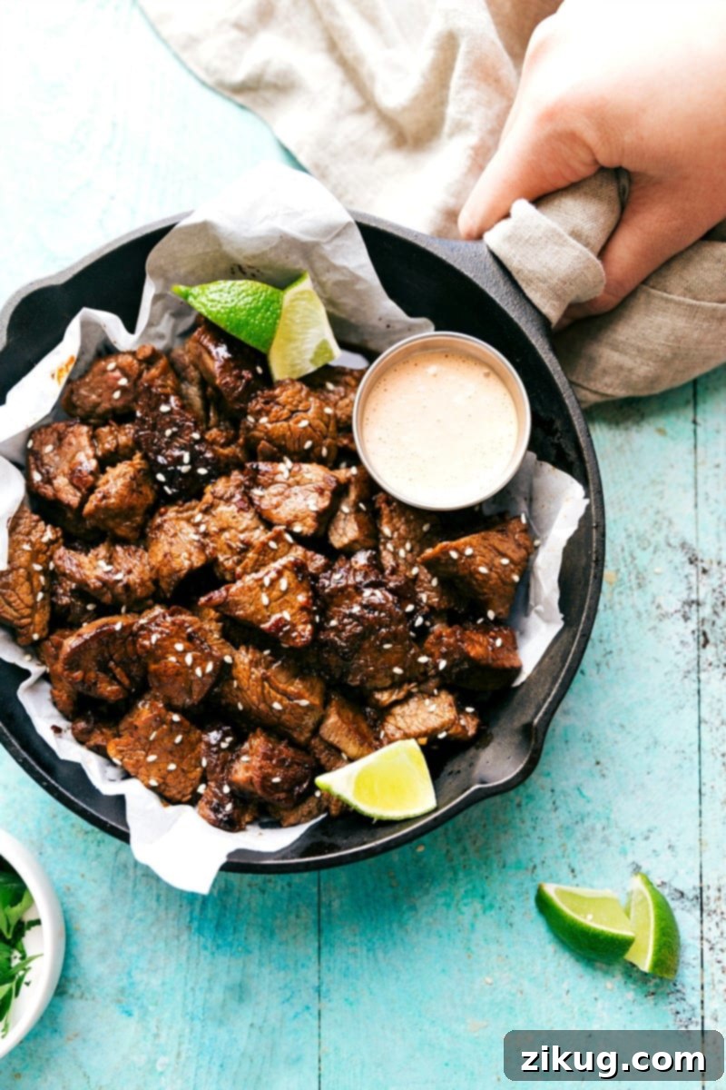 Try these Easy Asian Steak Bites--so easy and so delicious! Overhead view of Easy Asian Steak Bites searing in a skillet, alongside a small bowl of dipping sauce.