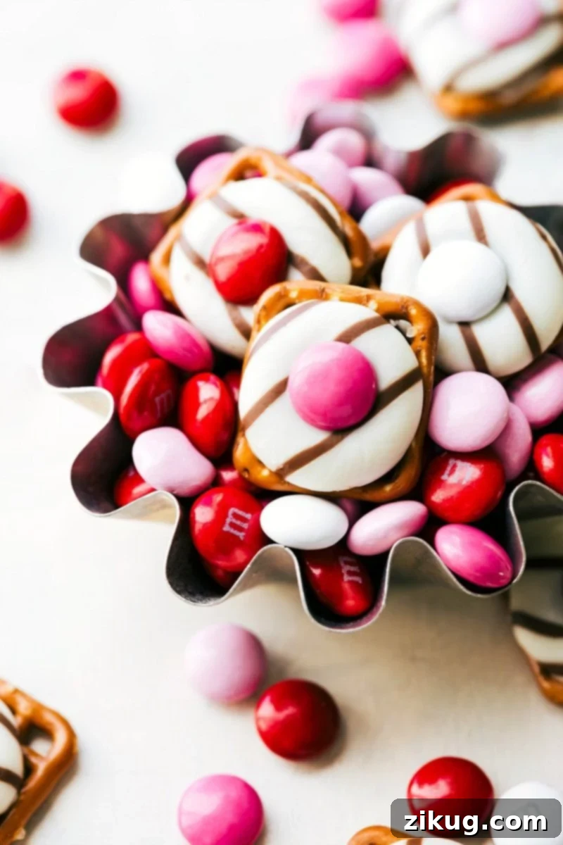 Sweet & Simple: 4 Valentine's Day Delights 3 A top-down shot of several Heart Hug Pretzels arranged neatly on a serving tray. Each pretzel is topped with a melted chocolate Hug and a red or pink Valentine's Day M&M, creating a vibrant and festive appearance. The background is softly blurred, emphasizing the delicious details of the treats, ready for a Valentine's celebration.