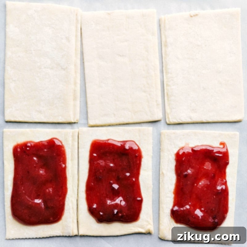 Preparing Homemade Toaster Strudels: Puff Pastry with a Heart of Strawberry Jam Puff pastry rectangles laid out, each with a generous dollop of rich strawberry jam in the center, ready for assembly.