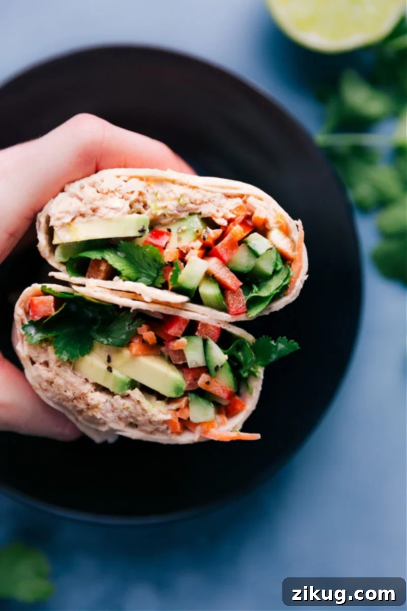 A vibrant and delicious Tuna Salad Wrap, artfully sliced in half to showcase its abundant, colorful, and appealing filling of creamy Sriracha tuna and crisp, fresh vegetables, ready to be enjoyed.