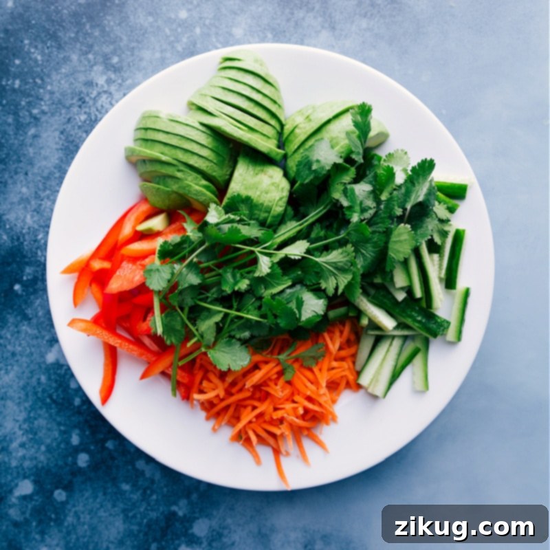 An inviting overhead view showcasing the fresh, colorful add-ins for Spicy Sriracha Tuna Salad Wraps: vibrant red bell pepper strips, finely shredded carrots, crisp cucumber matchsticks, aromatic cilantro, and creamy, thinly sliced avocado, all prepped and ready for assembly.