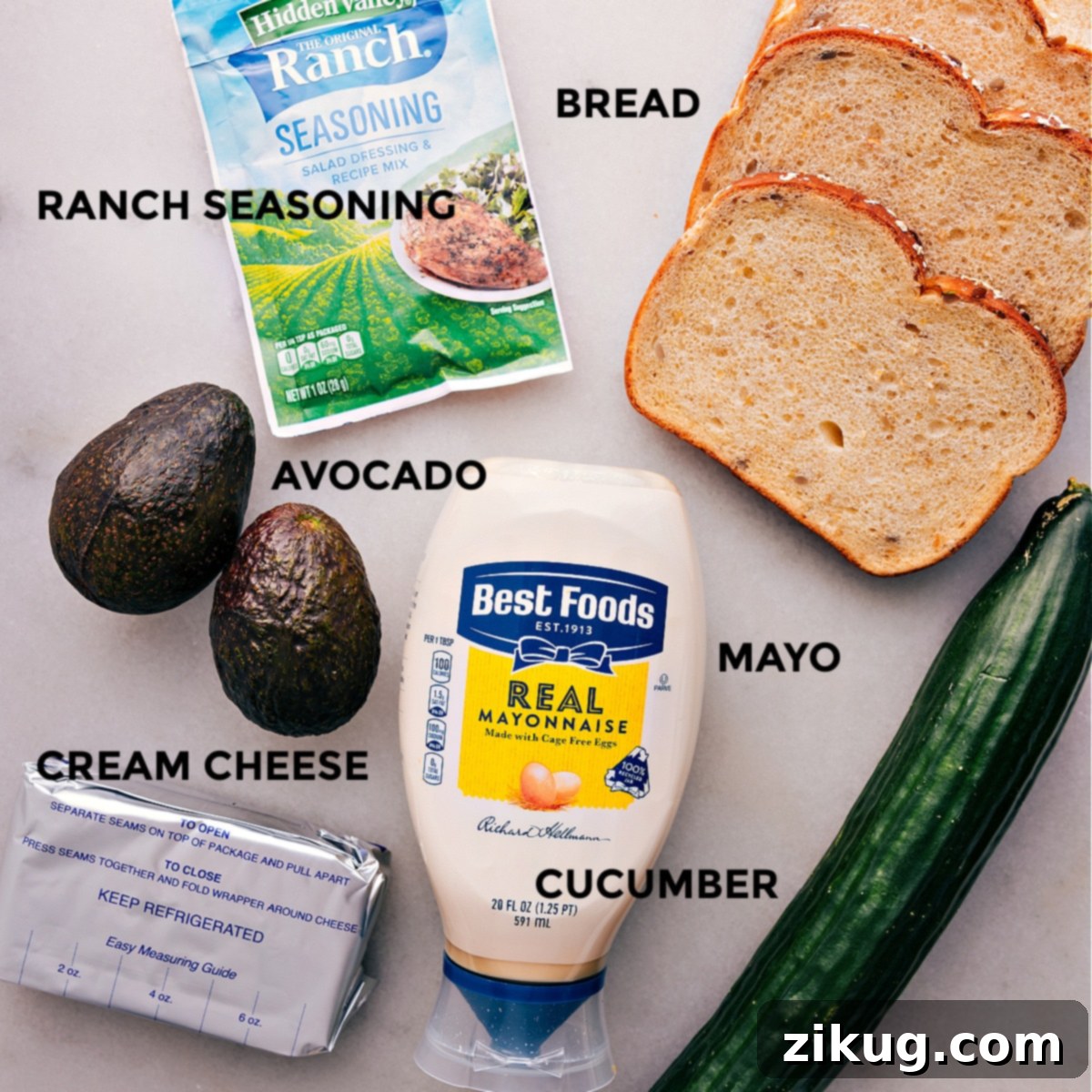 All fresh ingredients for the avocado sandwich recipe, including wheat bread, a bowl of ranch seasoning, crisp vegetables, creamy mayo, and softened cream cheese, neatly prepped for assembly.