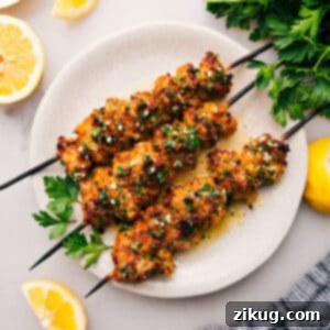 A plate of golden, crispy Chicken Spiedini skewers, drizzled with lemon garlic butter sauce and garnished with fresh parsley.