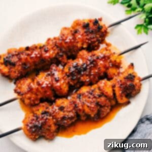 Close-up of crispy hot honey chicken skewers on a serving plate with a drizzle of sauce.