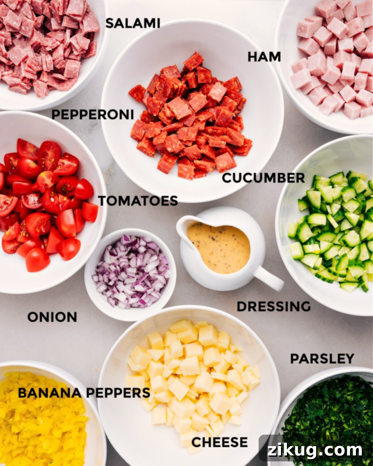 Ingredients In Italian Grinder Pasta Salad Recipe All the fresh ingredients for Italian Grinder Pasta Salad are neatly prepped on a cutting board: colorful meats, sliced cucumber, halved tomatoes, diced onion, and banana peppers, alongside a jar of dressing, cheese, and fresh parsley.