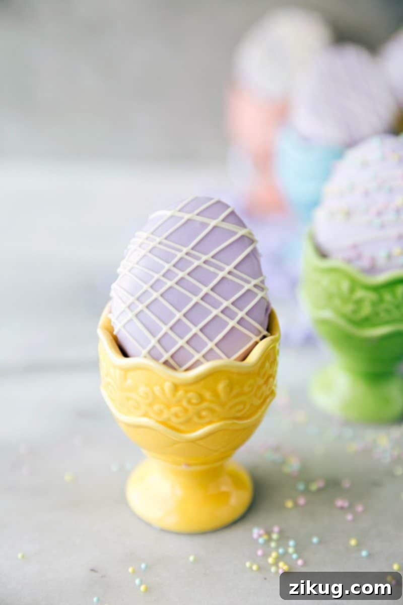 Elegant Mini Egg Petit Fours, small cakes coated in smooth frosting and decorated with white chocolate designs, perfect for a refined Easter dessert.