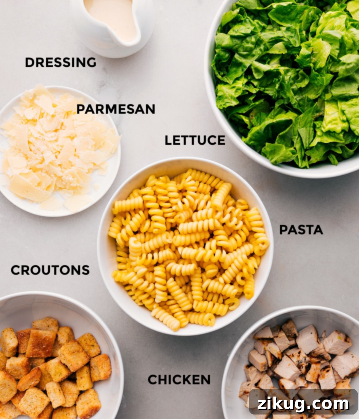 Ingredients In Chicken Caesar Pasta Salad All the fresh and flavorful ingredients for this delectable Chicken Caesar Pasta Salad, including a bowl of creamy dressing, grated Parmesan cheese, crisp romaine lettuce, perfectly cooked pasta, shredded chicken, and golden croutons, meticulously prepped and arranged for effortless assembly.