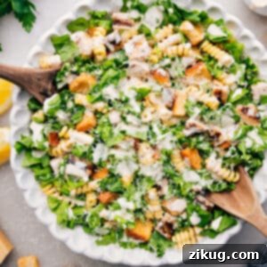 A serving of delicious Chicken Caesar Pasta Salad in a bowl, showing the mix of pasta, chicken, and lettuce with creamy dressing and parmesan cheese on top.