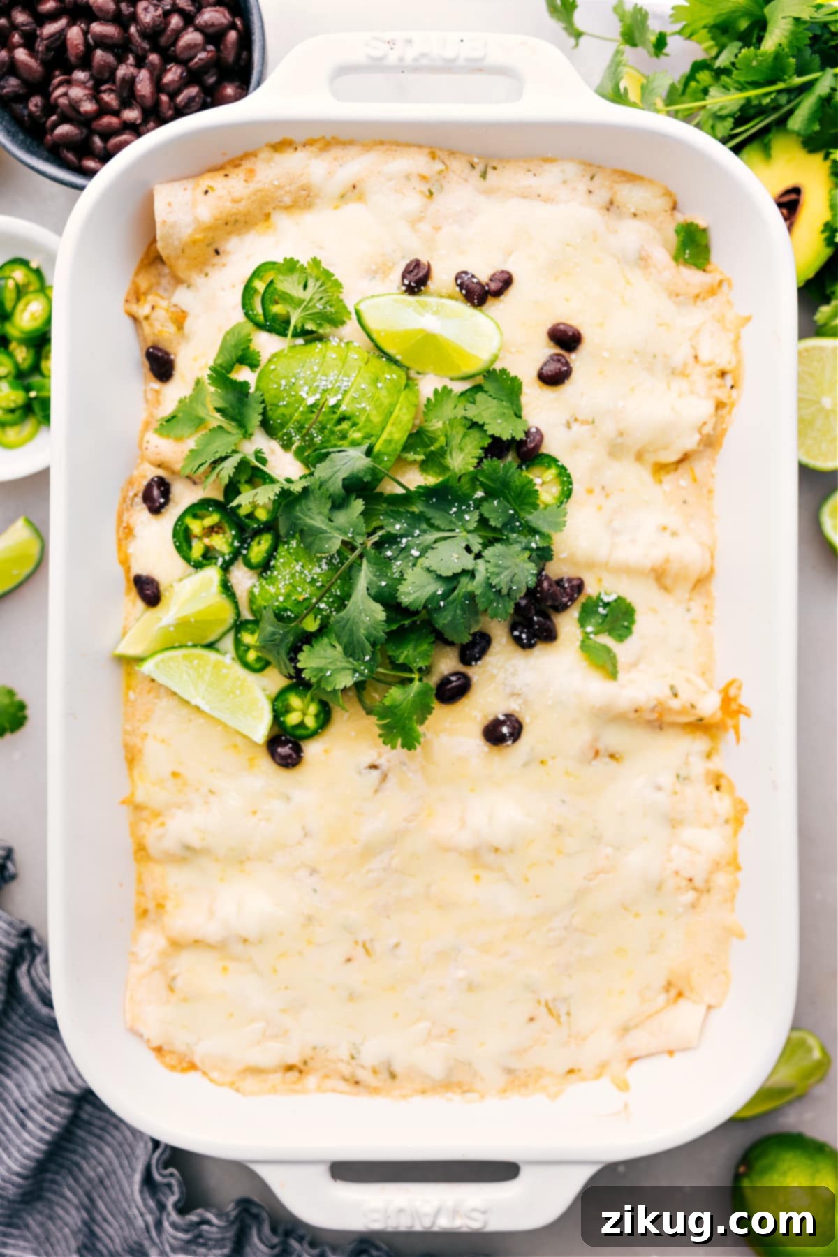 The Best White Chicken Enchiladas White Chicken Enchiladas in the casserole dish, topped with fresh cilantro, sliced jalapeños, lime wedges, and crumbled cotija, ready to serve.