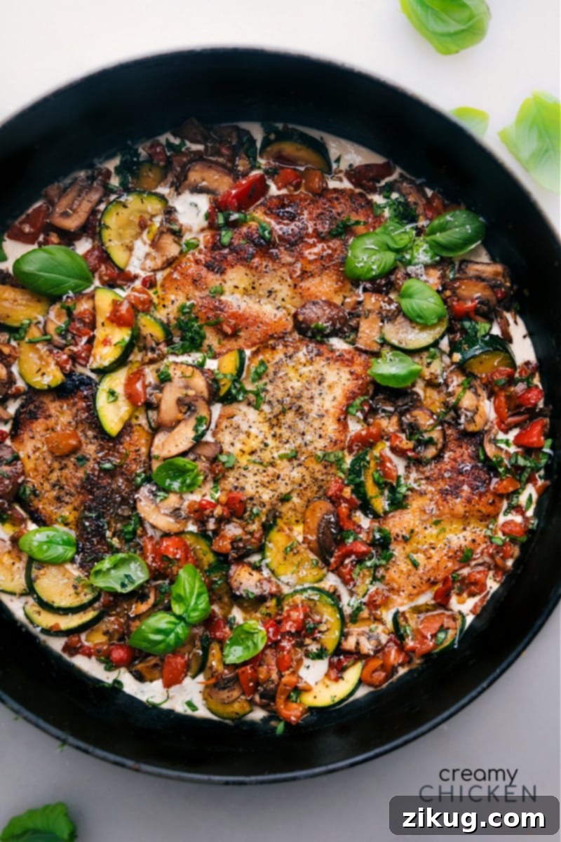 Overhead shot of a skillet filled with golden-brown creamy chicken and colorful vegetables, garnished with fresh basil and a lemon wedge, ready to be served.