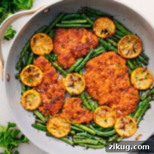 A plate of Lemon Parmesan Chicken with green beans and lemon slices.