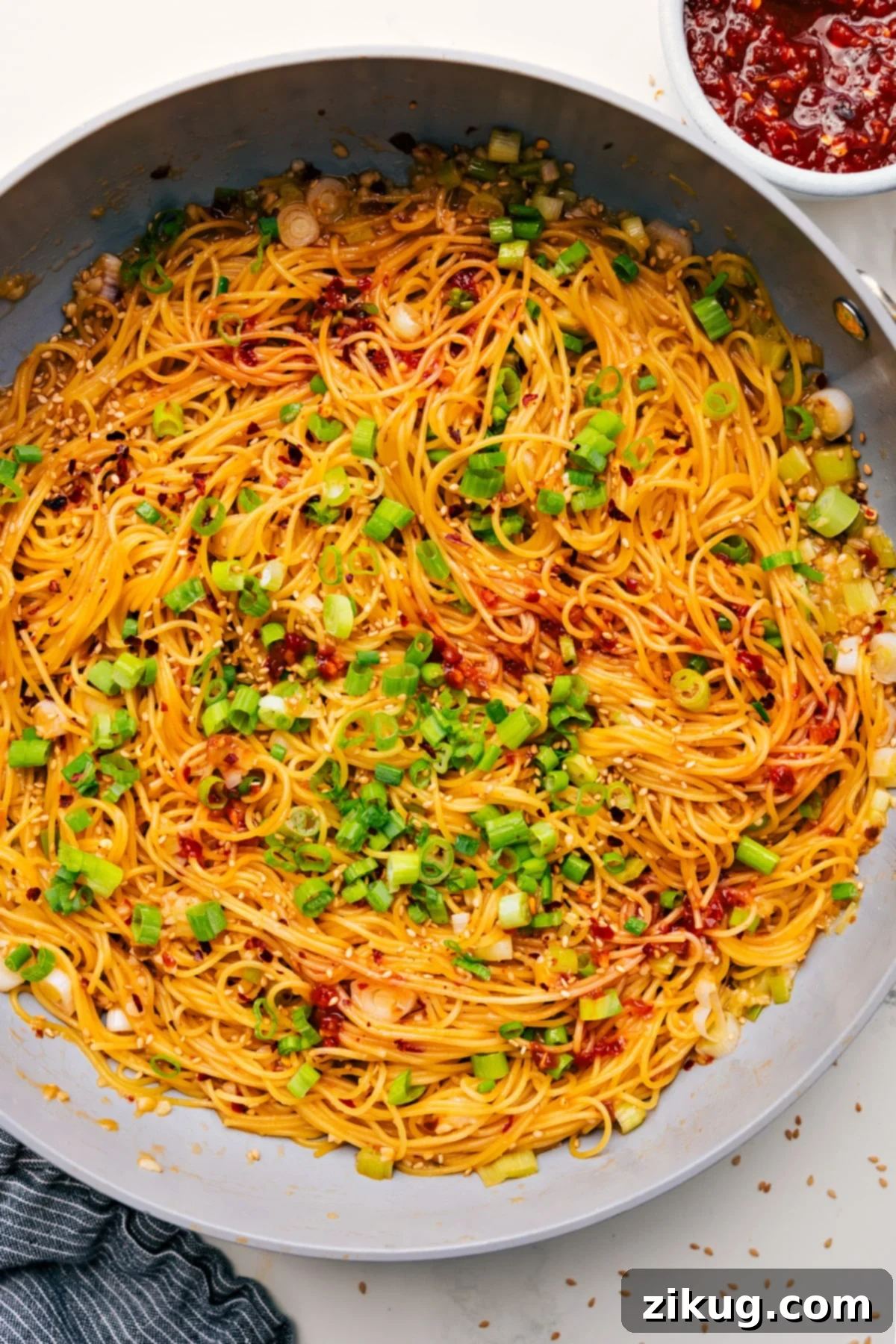 Flavorful And Delicious Chili Garlic Noodles Recipe A close-up of vibrant Chili Garlic Noodles in a skillet, generously garnished with fresh green onions and toasted sesame seeds, ready to be served.