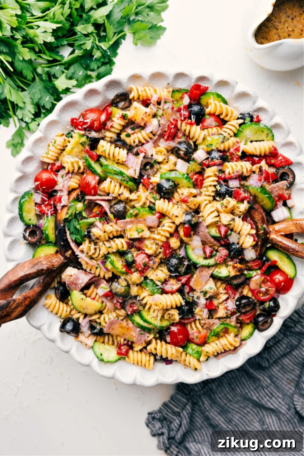 Delicious Italian Pasta Salad Recipe for Summer Gatherings A vibrant Italian Pasta Salad served in a large white bowl, featuring colorful rotini pasta, cherry tomatoes, black olives, green cucumber, red onion, roasted red peppers, tender chicken pieces, and salami, all generously coated in a rich Italian dressing. Fresh parsley garnishes the top.