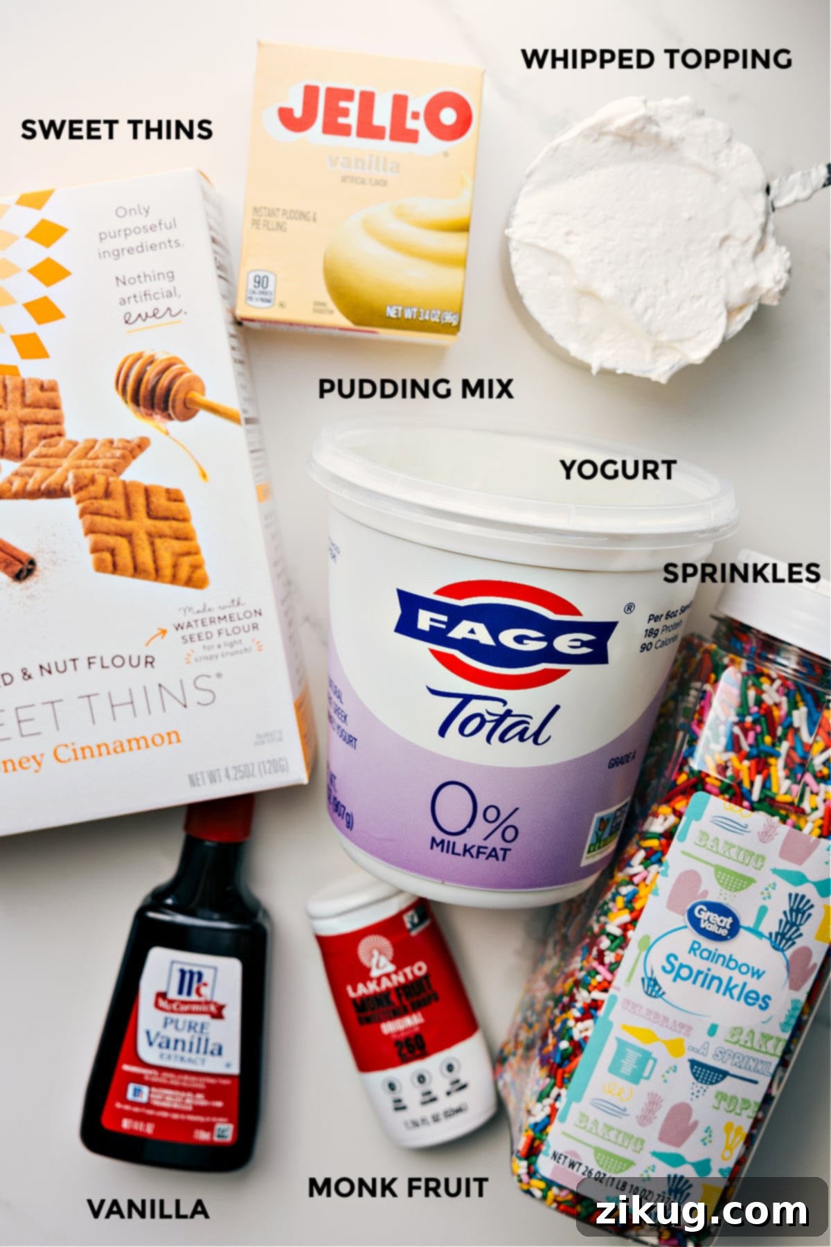 All the essential ingredients meticulously prepped for easy assembly of fluffy yogurt, including a bowl of creamy Fage Greek yogurt, a bottle of liquid monk fruit sweetener, a small bowl of vanilla extract, a packet of instant vanilla pudding mix, a container of thawed whipped topping, a vibrant bowl of colorful sprinkles, and golden graham crackers for dipping.