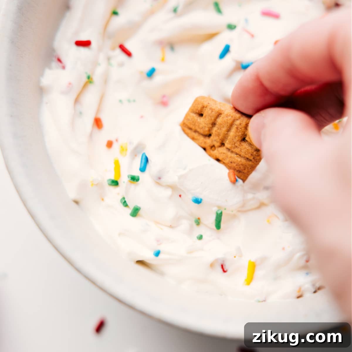 A vibrant bowl of Funfetti-flavored fluffy yogurt, generously adorned with colorful sprinkles. A crisp graham cracker is delicately dipped into the creamy mixture, highlighting its rich texture and serving as a perfect accompaniment, inviting you to take a bite.