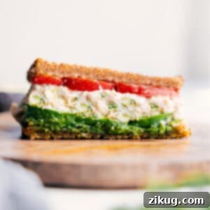 A perfectly sliced Tunacado sandwich, showcasing the layers of tuna, pesto, avocado, and tomato on toasted bread.