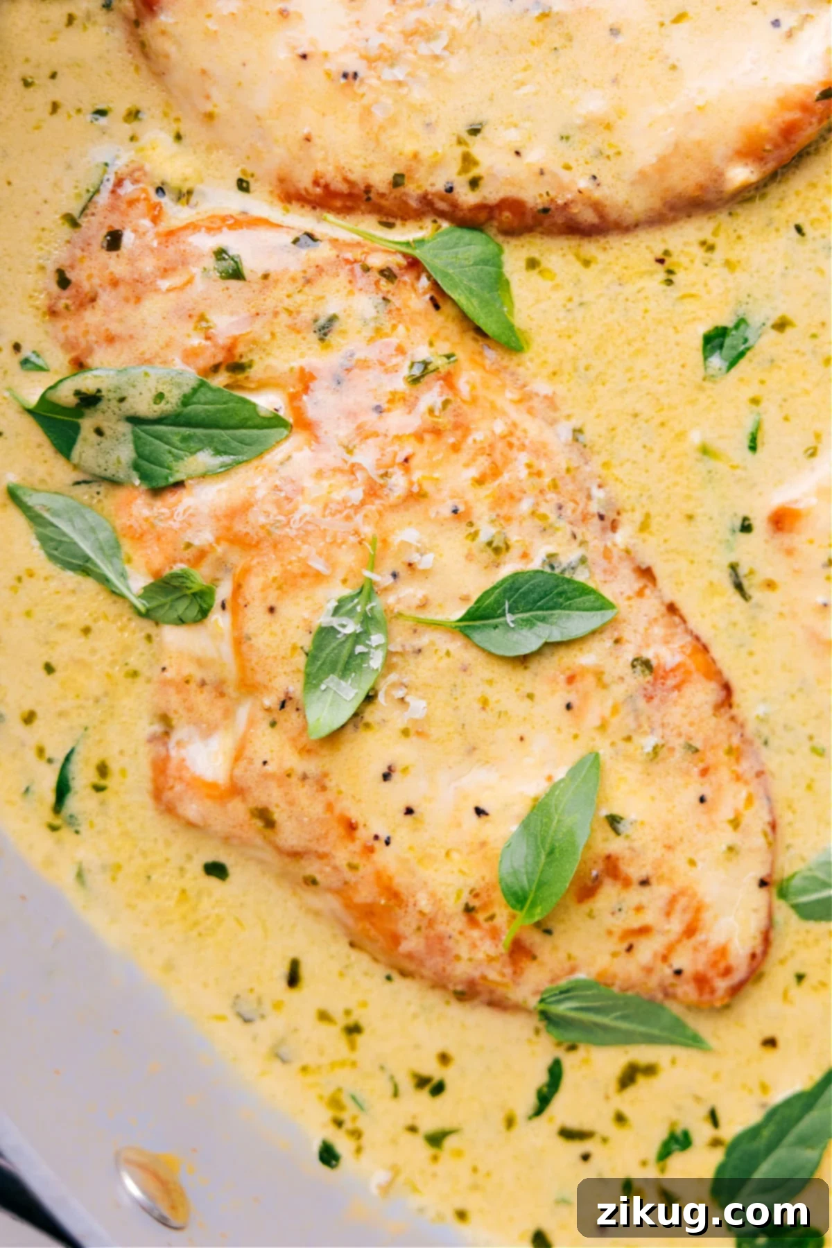 Golden-brown creamy pesto chicken simmering in a rich green sauce in a cast iron skillet, garnished with fresh basil leaves.