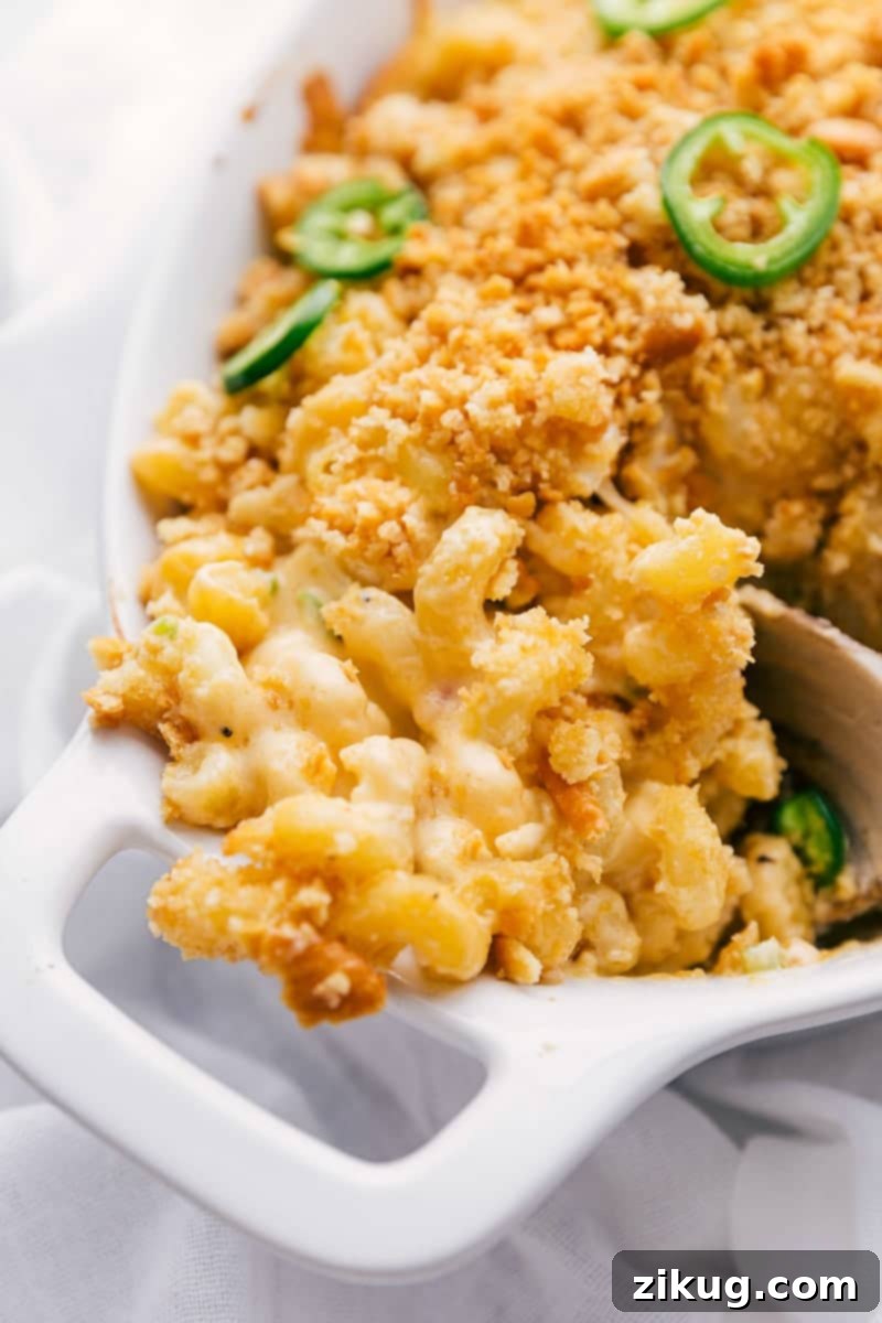 A generous serving of Jalapeño Popper Mac & Cheese, rich with melted cheese, crispy bacon, and bright green jalapeños, being scooped from a baking dish.
