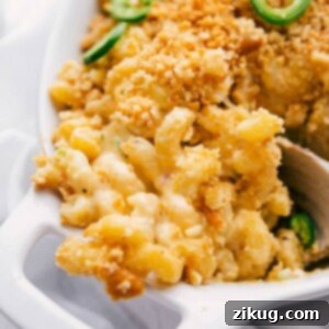 A close-up of the finished Jalapeño Popper Mac and Cheese in a baking dish, with a scoop removed, showcasing its cheesy, spicy layers and golden topping.