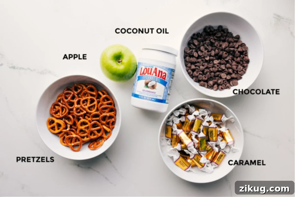 All the essential ingredients for Caramel Apple Bark, including chocolate chips, coconut oil, mini pretzels, a Granny Smith apple, soft caramels, and heavy cream, neatly prepped for assembly.