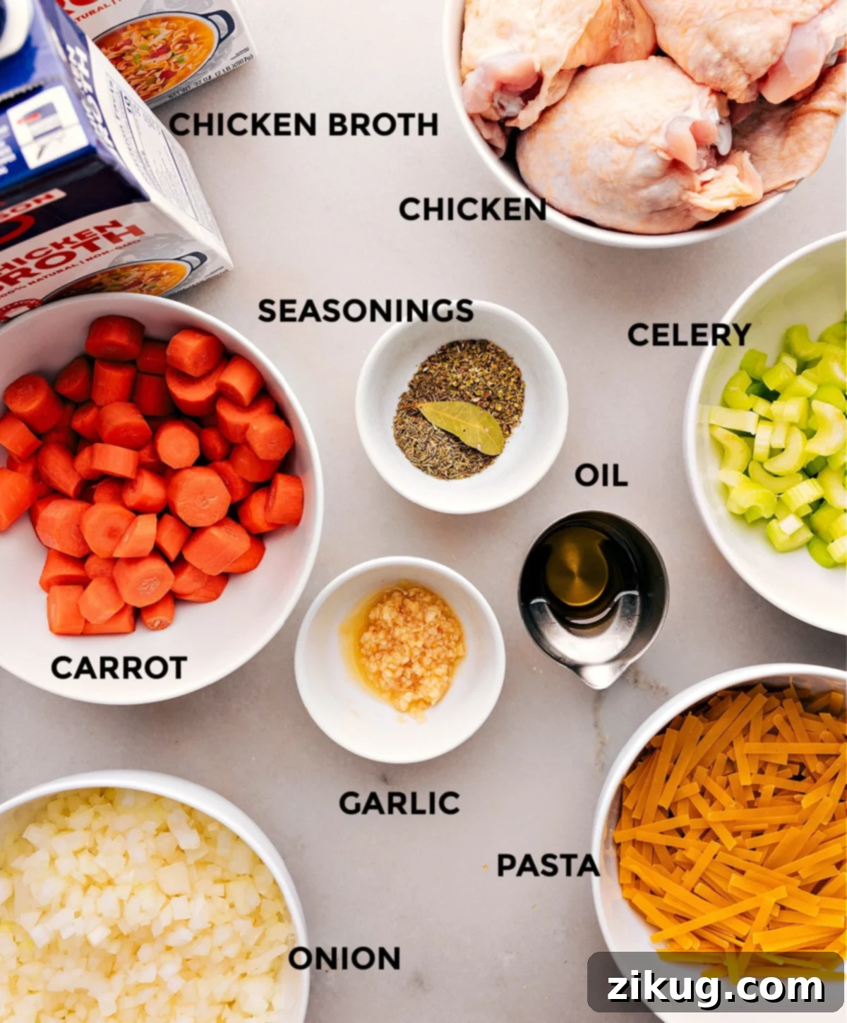 Ingredients For The Best Chicken Noodle Soup All the fresh ingredients, including chicken thighs, carrots, celery, onion, garlic, herbs, and noodles, neatly arranged on a wooden board before cooking.