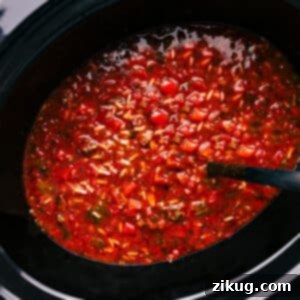 A bowl of Crockpot Stuffed Pepper Soup, garnished with fresh parsley and shredded cheddar cheese, with a spoon ready to dive in.