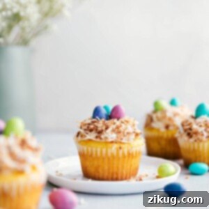 A yellow cupcake with cream cheese frosting, toasted coconut, and M&M's in a bird's nest style.