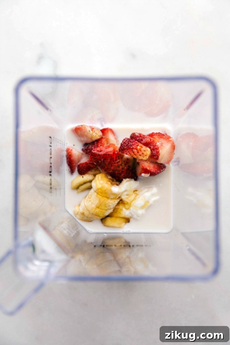 Gather your wholesome ingredients for a quick and nutritious Strawberry Banana Smoothie. This image showcases unsweetened almond milk, creamy honey vanilla Greek yogurt, perfectly ripe bananas (ready for freezing), luscious frozen strawberries, and a touch of golden honey to sweeten. Overhead shot of all five essential ingredients for a Strawberry Banana Smoothie: almond milk, Greek yogurt, ripe bananas, honey, and fresh strawberries, laid out before blending.