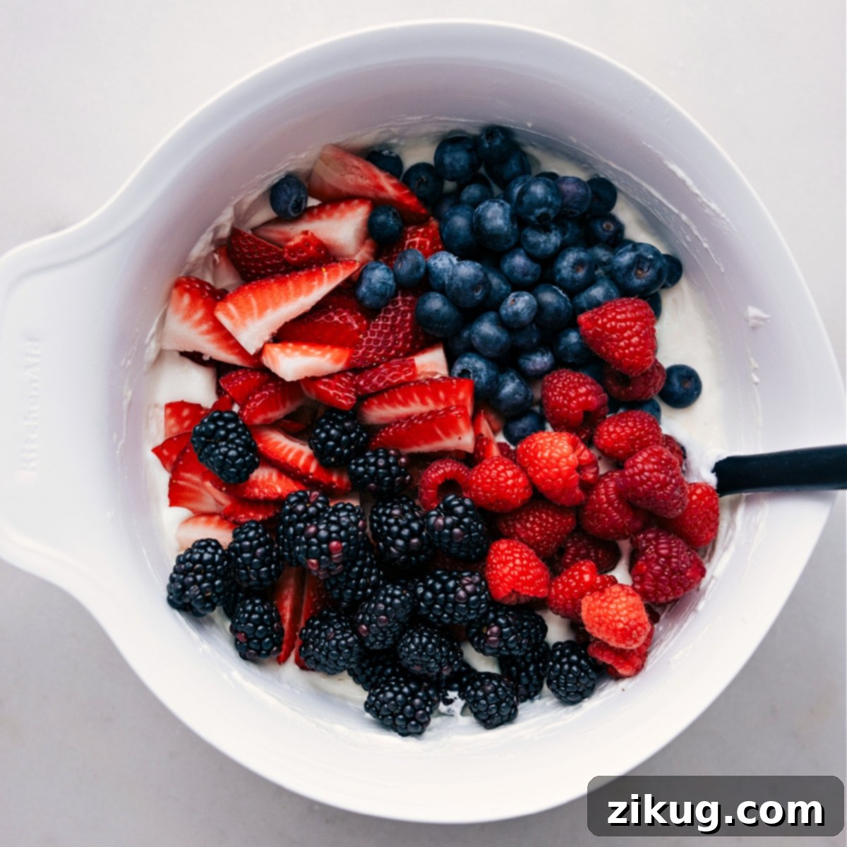 A beautifully presented bowl of Berry Cheesecake Salad on a rustic wooden table, with a serving spoon.
