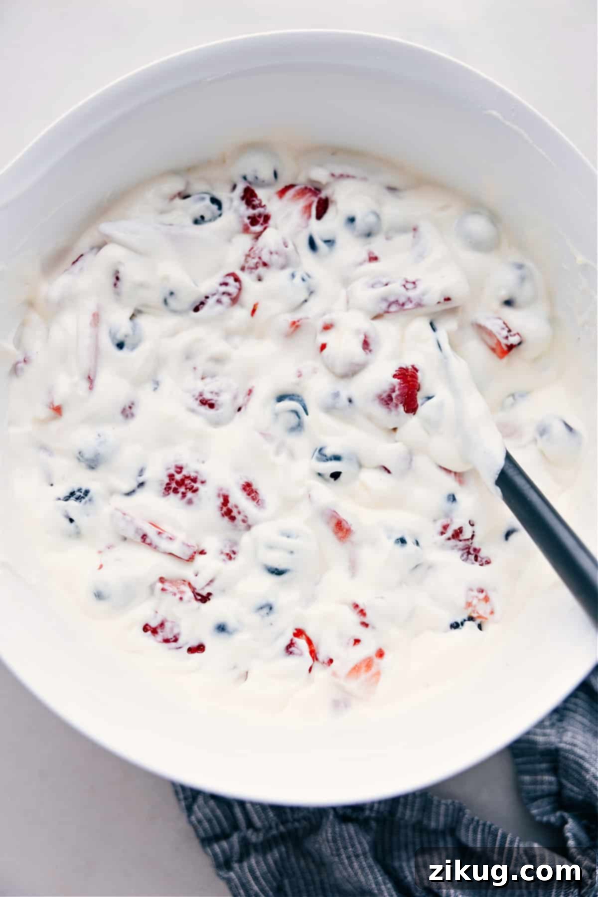 An overhead shot showcasing the vibrant medley of fresh berries generously coated in creamy cheesecake dressing in a clear glass bowl.