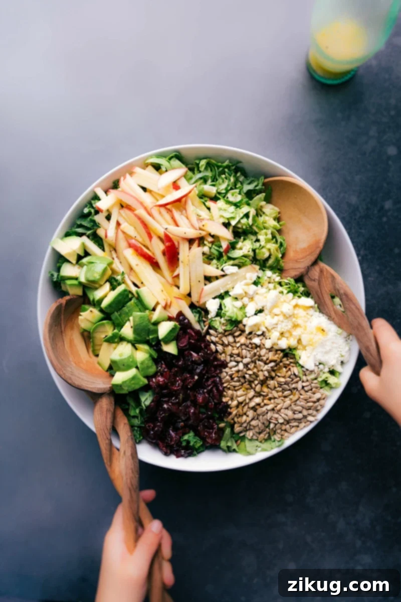 A vibrant Brussels sprout salad in a large bowl, brimming with shredded sprouts, kale, apple slices, red cranberries, sunflower seeds, and crumbled feta cheese, all glistening with a fresh dressing. Delicious and healthy toppings are beautifully arranged.