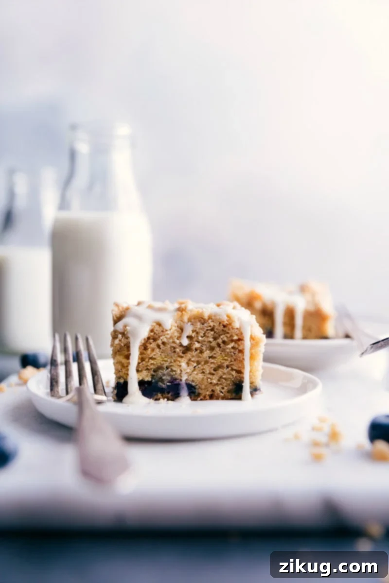 This moist and flavorful Blueberry Coffee Cake with a hint of lemon is topped with a sweet streusel and simple lemon glaze. A perfect treat for any occasion. #easy #lemon #buttermilk #withcrumbtopping #recipes #recipeseasy #best #blueberry #coffee #cake A delectable slice of Blueberry Coffee Cake with streusel and lemon glaze on a white plate, ready to be enjoyed.