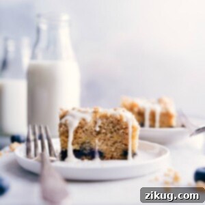 A perfectly baked slice of blueberry coffee cake with a generous streusel topping and lemon glaze, presented on a plate.