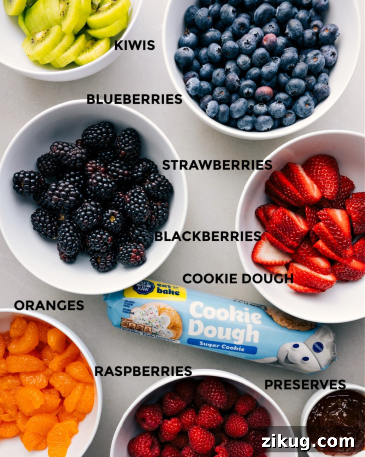 Fresh ingredients laid out for fruit pizza assembly: vibrant fruits, ready-to-use cookie dough, and glossy fruit preserves, simplifying the process.