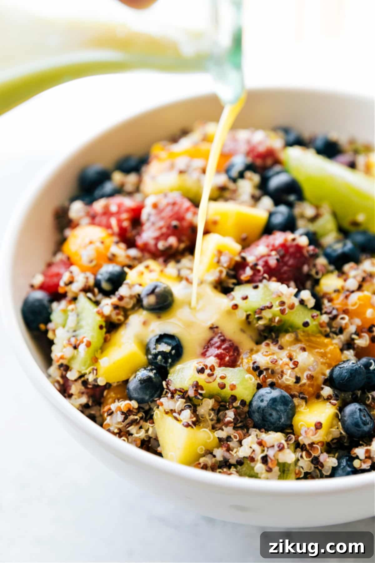 Our Favorite Quinoa Fruit Salad, Perfectly Dressed Our Favorite Quinoa Fruit Salad being dressed with a generous pour of the citrus vinaigrette, highlighting its fresh appeal.