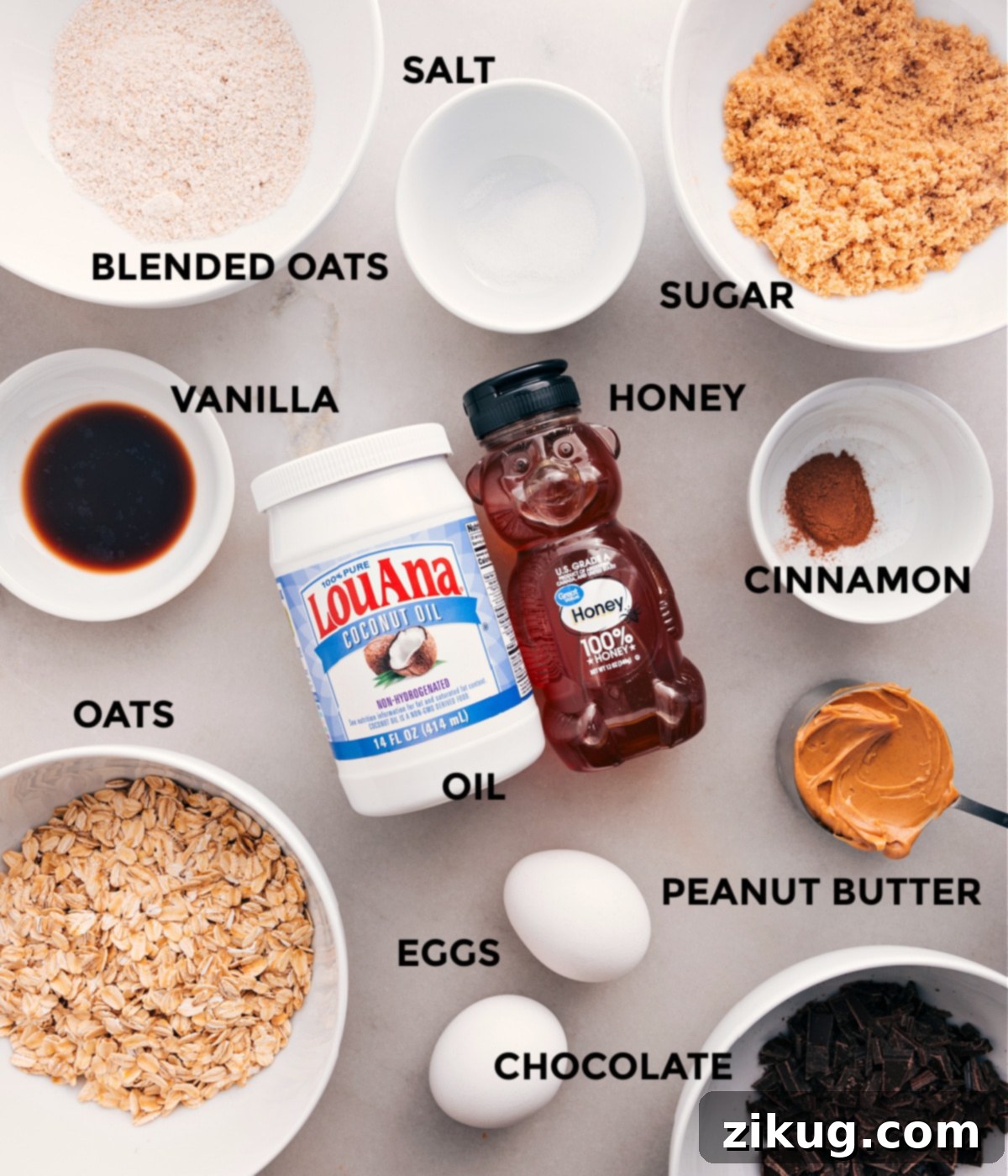 A neatly arranged spread of all key ingredients for making Soft-Baked Oatmeal Breakfast Bars, including old-fashioned oats, oat flour, cinnamon, salt, peanut butter, coconut oil, honey, brown sugar, vanilla extract, eggs, and dark chocolate chips.