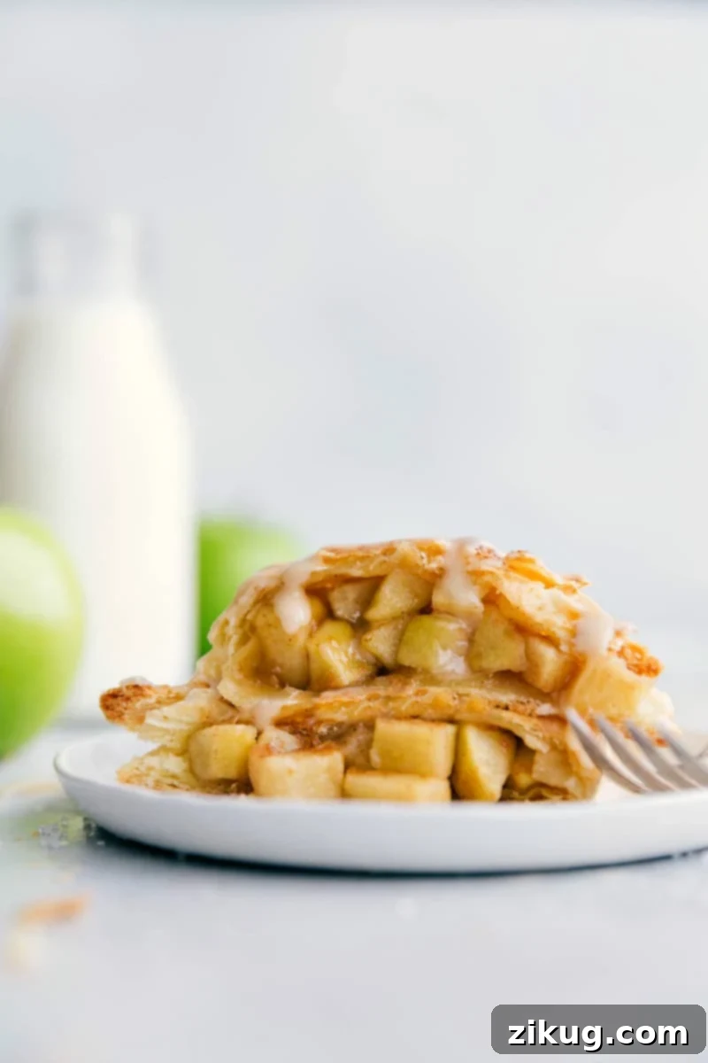 Best Easy Apple Turnover Recipe with Puff Pastry Two halves of a golden-brown apple turnover stacked, showcasing its flaky layers and generous apple filling, drizzled with a sweet glaze.