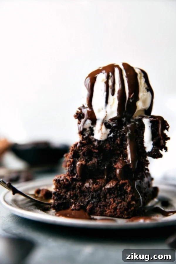 Indulge in these double-chocolate, super fudgy applesauce brownies, expertly crafted with no oil, no butter, and no refined flour. The best part? There are no unexpected vegetables or beans hidden inside, just pure, satisfying chocolate goodness! This healthy, quick, and easy recipe from Chelseasmessyapron is a better-for-you dessert perfect for any occasion. Applesauce Brownies topped with vanilla ice cream and drizzled with chocolate syrup, served on a rustic plate.