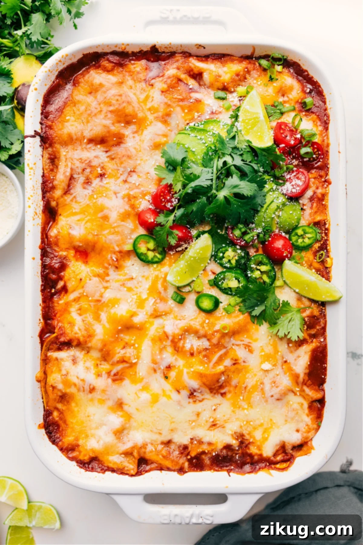Chicken Enchilada Casserole just out of the oven, topped with fresh cilantro, diced avocado, chopped tomatoes, and lime wedges.
