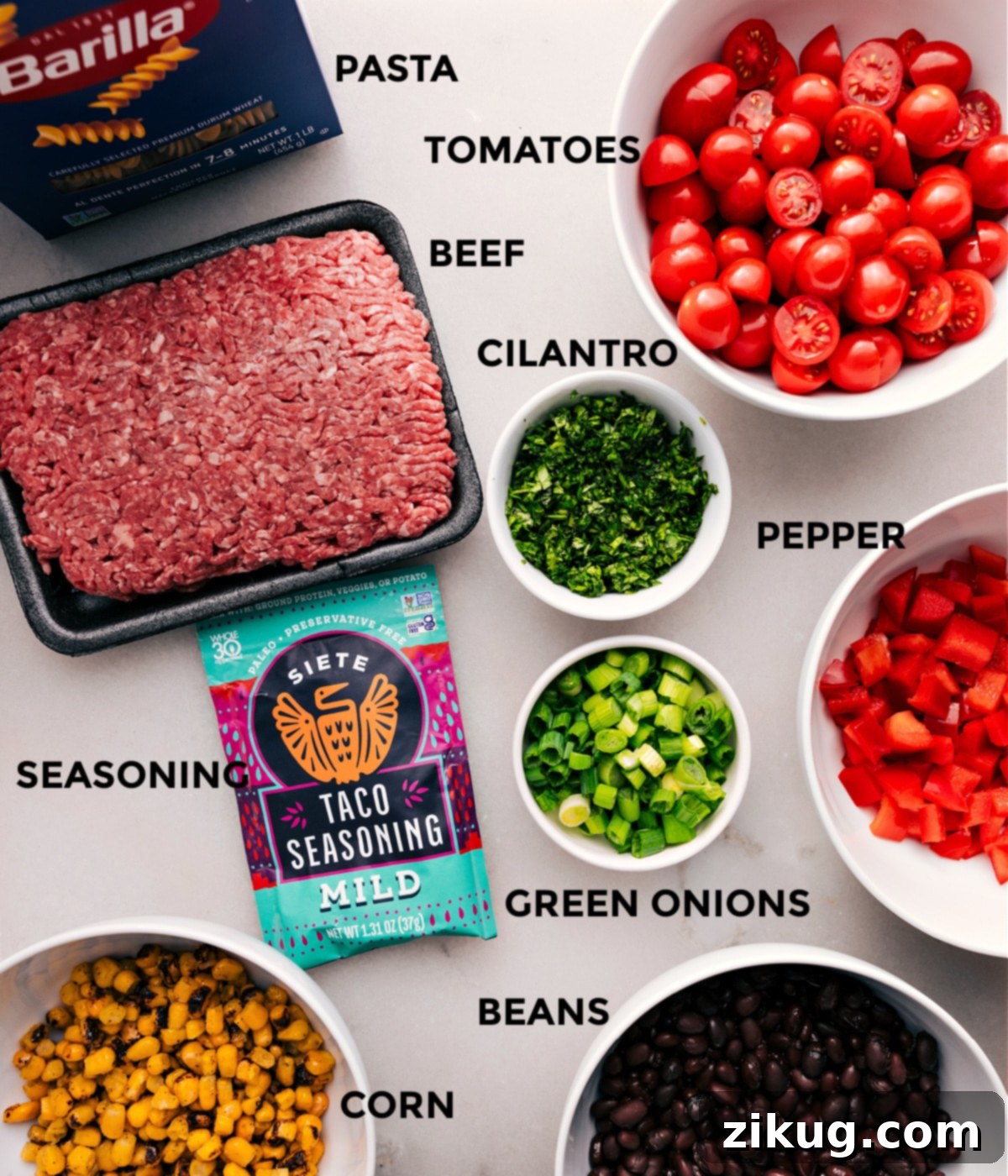 A colorful array of fresh ingredients for Taco Pasta Salad, including cooked rotini, seasoned ground beef, vibrant tomatoes, red bell pepper, green onions, cilantro, black beans, and corn, laid out on a wooden board.