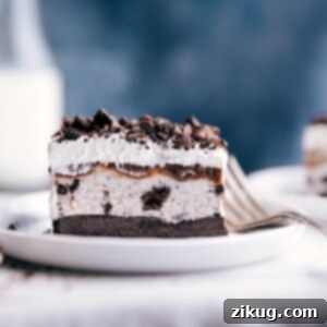 A delectable slice of Oreo ice cream cake, perfectly layered with cookie crust, ice cream, hot fudge, and whipped cream, presented on a white plate. This image is the main recipe visual.