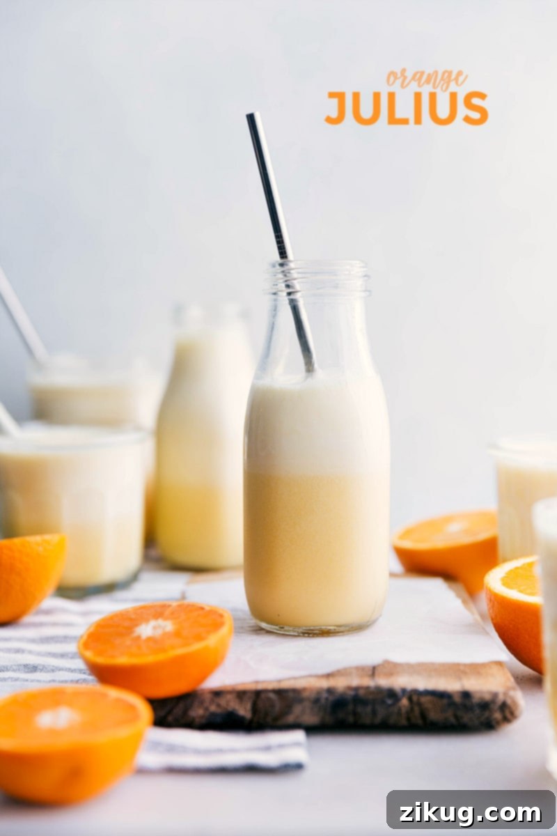 Two glasses of homemade Orange Julius, garnished with fresh orange slices, ready to be enjoyed. The bright, frothy drink evokes warmth and nostalgia.