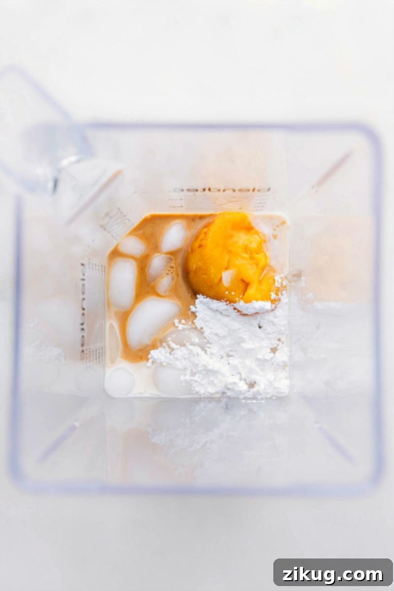 A blender being filled with the key ingredients for Orange Julius, including orange juice concentrate, milk, and ice cubes, highlighting the simplicity of preparation.