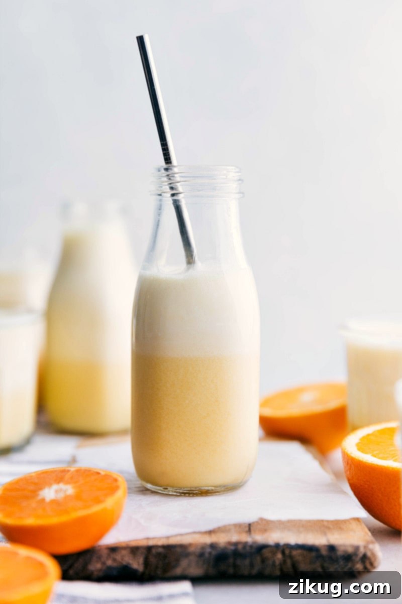 A vibrant Orange Julius drink in a clear glass with a straw, accompanied by artfully arranged fresh orange slices, ready for serving.