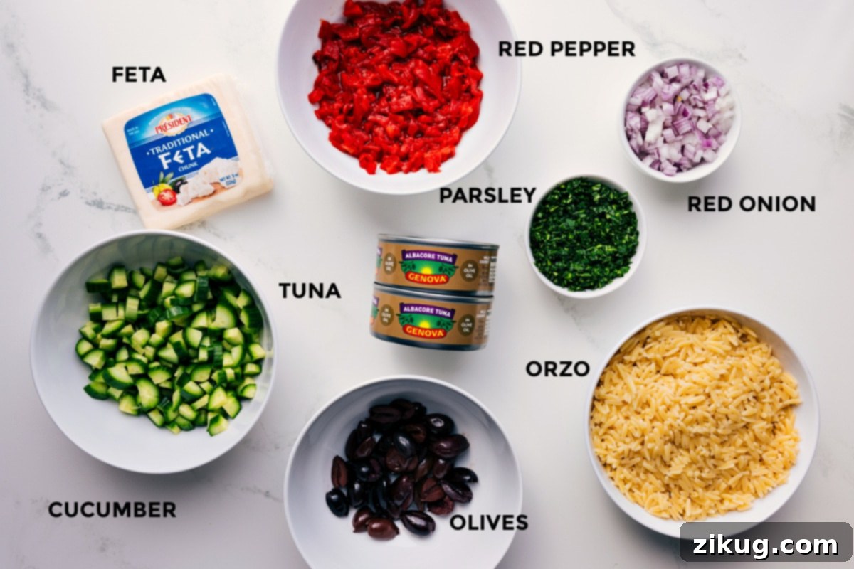All the vibrant ingredients for Mediterranean Tuna Salad prepped for easy assembly, including crumbled feta cheese, smoky roasted red pepper, tangy red onion, fresh parsley, perfectly cooked orzo, briny olives, olive-oil-packed tuna, and crisp cucumber.